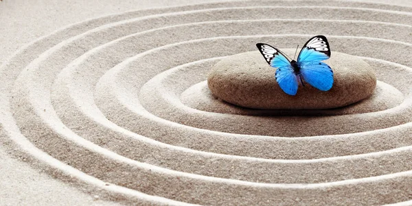 Zen bahçesi meditasyon taşı arka plan ve rahatlama dengesi ve ahenk ruhsallığı veya spa sağlığı için kumdaki taşlar ve çizgilerle kelebek..