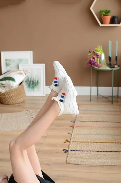 female sport legs in white denim shorts and white sneakers on a wooden background.