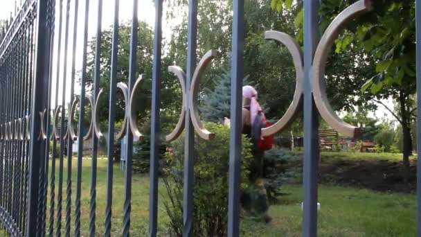 Seorang wanita dalam syal, gaun panjang dengan ransel berjalan melewati pagar — Stok Video