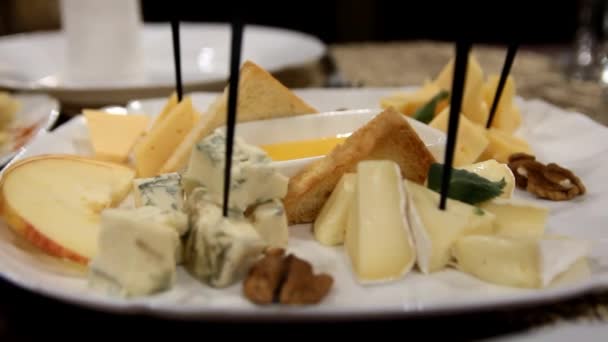 Pieces of different varieties of cheese and nuts lie on a white plate with adhesied — 图库视频影像
