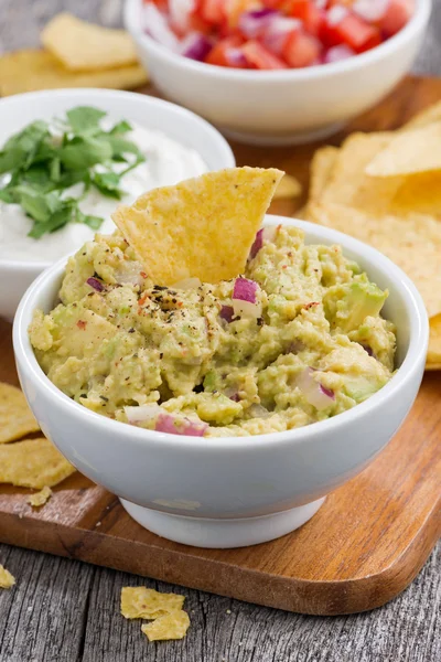 Omáčkou guacamole, tomatová salsa a kukuřičnými chipsy na dřevěném prkénku — Stock fotografie