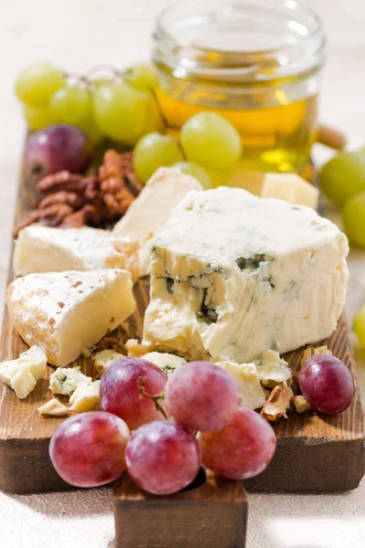 Planche à fromage, fruits et miel sur fond blanc, verticale — Photo