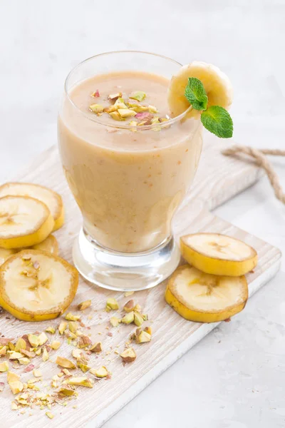 Frullato di banana in un bicchiere su tavola bianca, verticale — Foto Stock