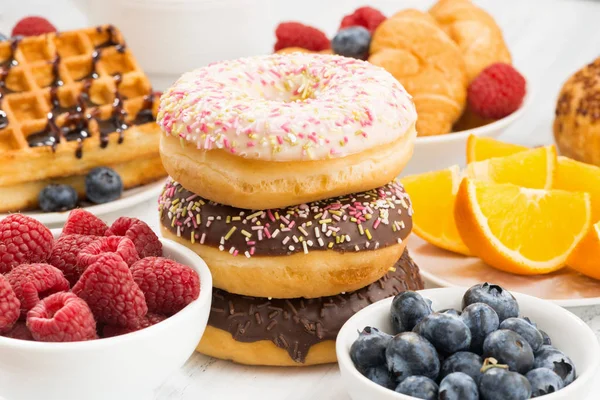 Rosquillas glaseadas, dulces y bayas frescas en la mesa, primer plano — Foto de Stock