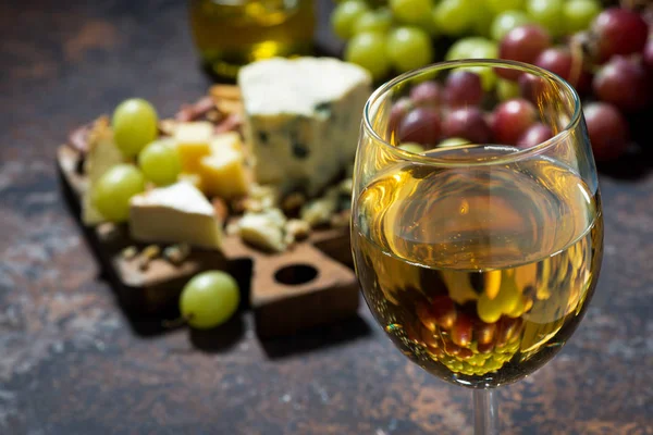 Glass of white wine, cheeseboard and fruit on dark background — Stock Photo, Image