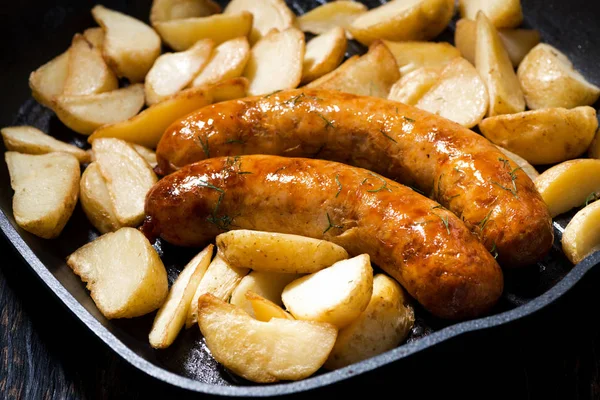 Fried pork sausages with potatoes in frying pan, closeup — Stock Photo, Image