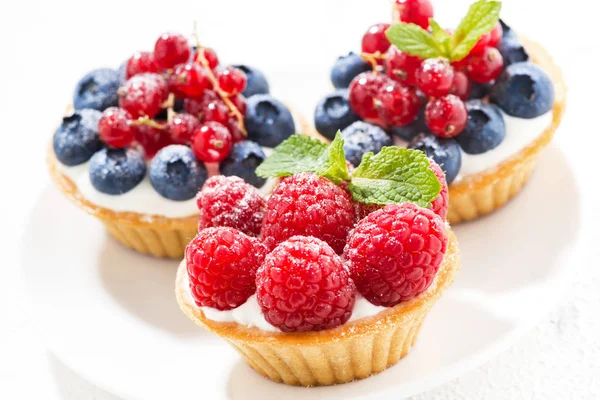 Mini taartjes met slagroom en verse bessen op witte achtergrond — Stockfoto
