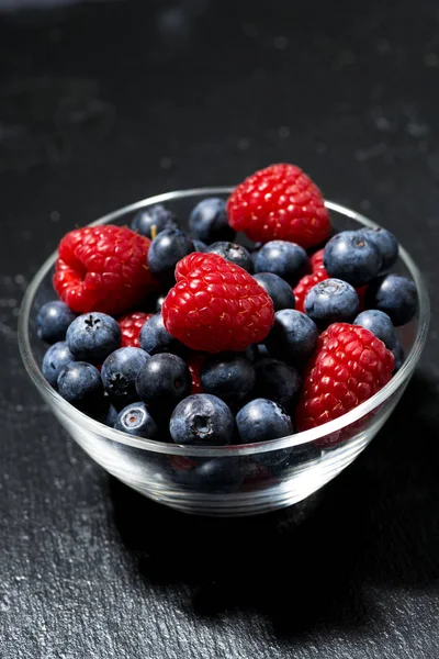 Frische Beeren in einer Glasschale auf dunklem Hintergrund, senkrecht — Stockfoto