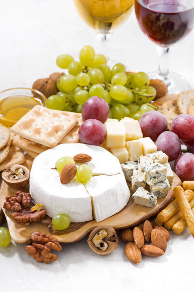 camembert, grapes, wine and snacks on a white table, vertical