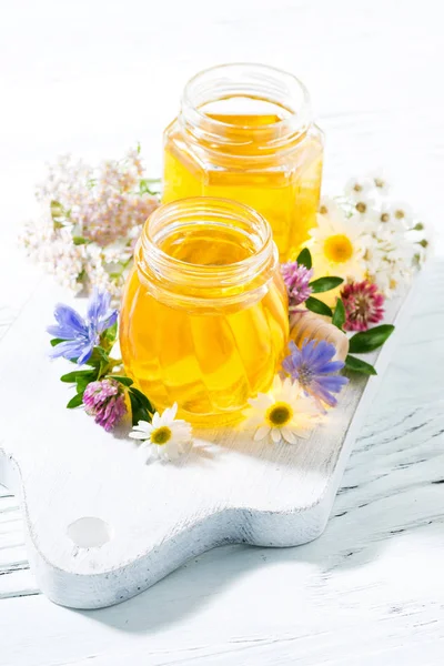 jars with fresh flower honey on white board, vertical