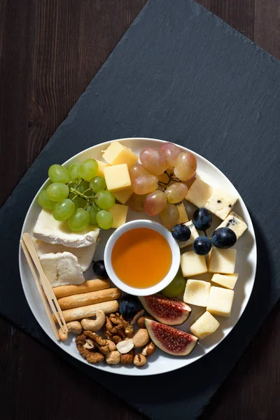 Prato de queijos, lanches e frutas em um fundo preto — Fotografia de Stock