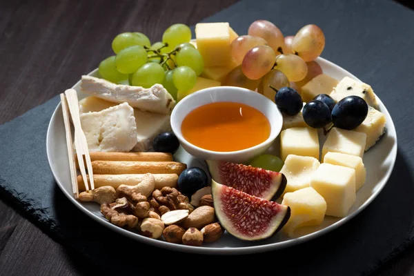 Plate of cheeses, snacks and fruits on a dark background — Stock Photo, Image
