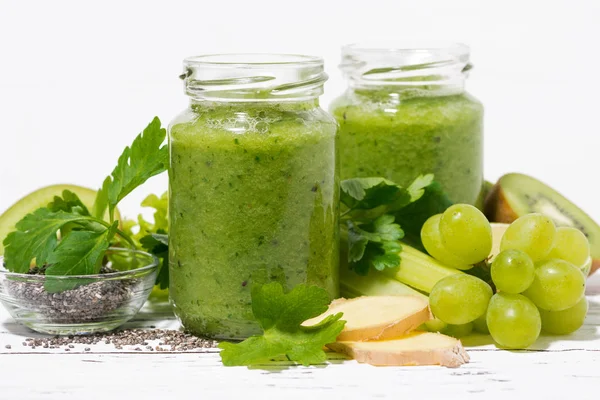 green fruit and vegetable smoothies in jars on white table