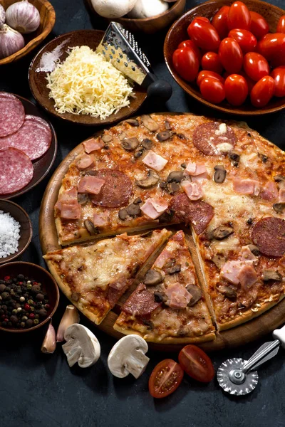 Pizza med salami och ingredienser på en svart bakgrund — Stockfoto