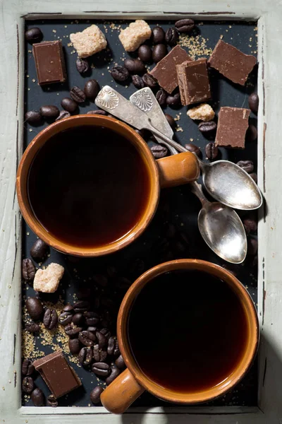 İki fincan sade kahve, şeker ve çikolata bir kara tahta üzerinde — Stok fotoğraf