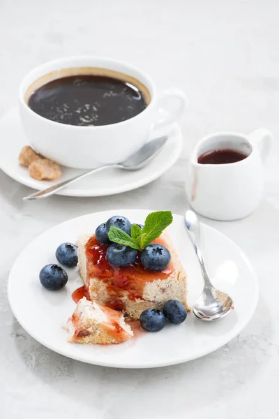 Piece of cheesecake with berry jam and cup of coffee — Free Stock Photo