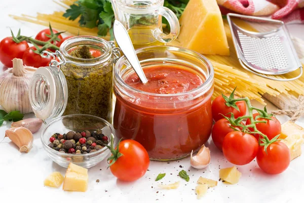 Salsa di pomodoro, pesto e ingredienti per la pasta su una tavola bianca — Foto Stock