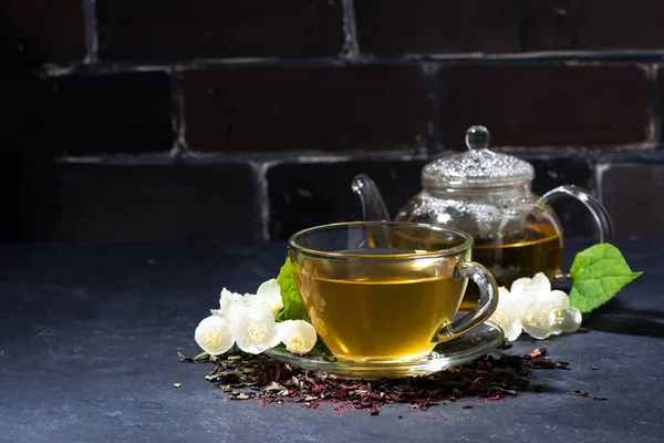 Чашка и чайник ароматного жасминового чая на темном фоне — стоковое фото