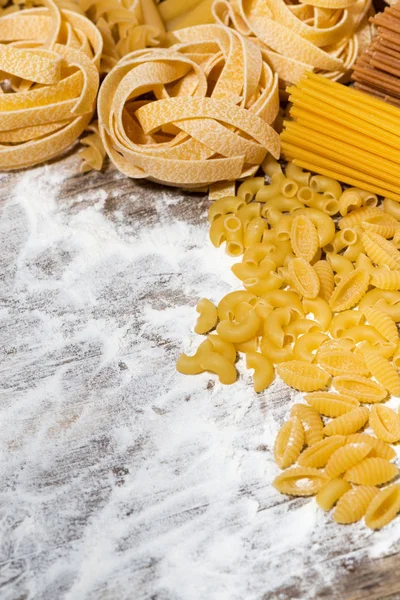Assortment of dry pasta on a wooden board with flour, top view — Stock Photo, Image