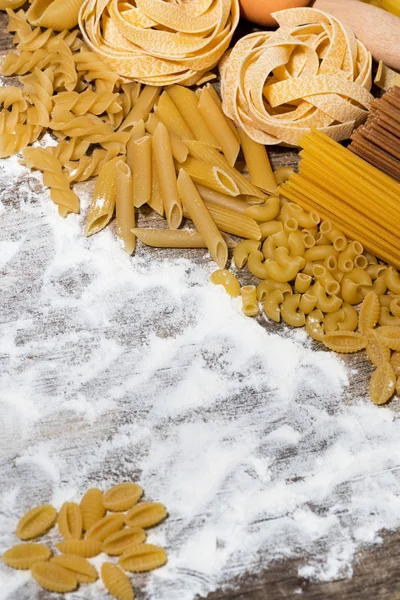 Diferentes pastas secas en una tabla de madera con harina, vertical — Foto de Stock