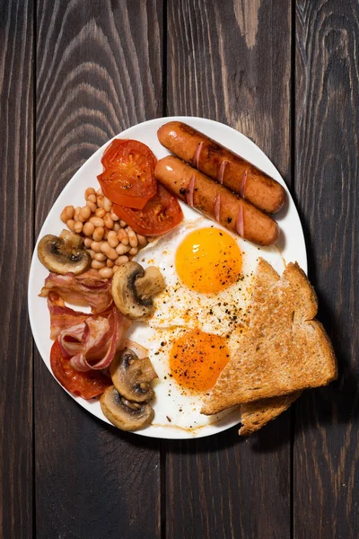 Смажені яйця з беконом, ковбасками та овочами на дерев'яному столі — стокове фото