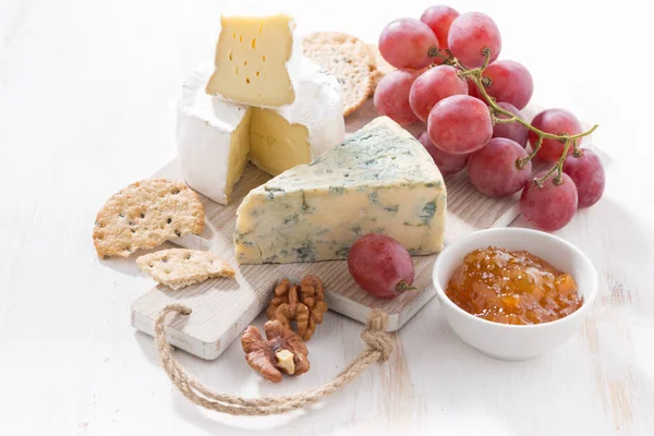 Molded cheeses, fruit and snacks on a white wooden board — Stock Photo, Image