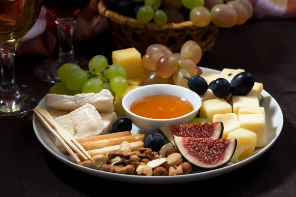 Plate of cheeses, snacks and wine on a dark background — Stock Photo, Image