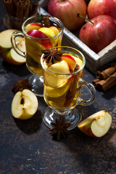 glasses of hot apple tea with spices on dark table, vertical 