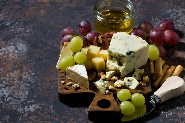 チーズの盛り合わせ、新鮮な果物や暗い背景の上に蜂蜜 — ストック写真