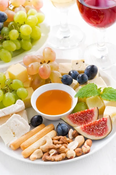 cheeses, fresh fruits, wine and snacks on plate, vertical
