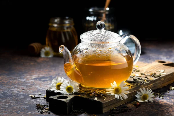 Glass teapot of fragrant chamomile tea on dark background — Stock Photo, Image