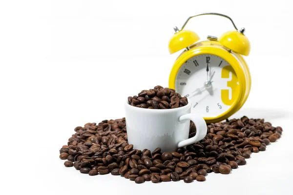 Taza con granos de café y reloj despertador amarillo sobre fondo blanco — Foto de Stock