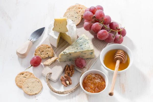 Molded cheeses, fruit and snacks on a white wooden board — Stock Photo, Image