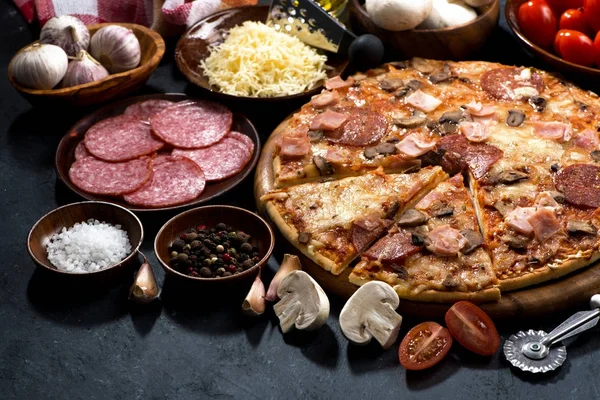 Pizza med salami och ingredienser på en mörk bakgrund — Stockfoto