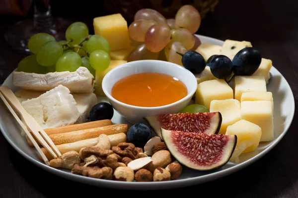 Plate of cheeses, snacks and fruits on a dark background — Stock Photo, Image