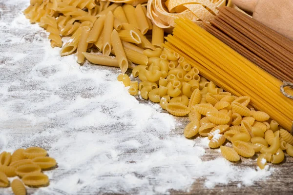 Different dry pasta on a wooden board with flour — Stock Photo, Image