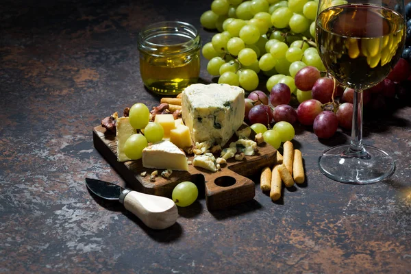 Cheeseboard, fruit and glass of white wine on a dark background — Stock Photo, Image