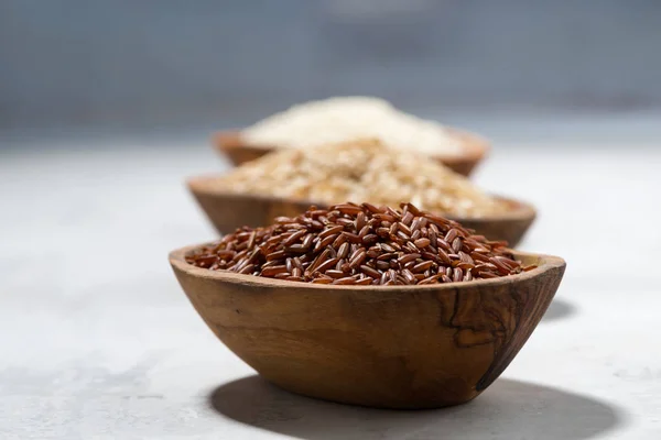 Três tipos de arroz seco em tigelas de madeira — Fotografia de Stock