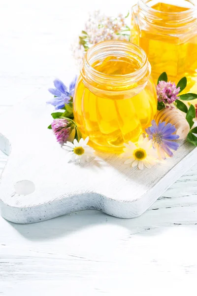 Jarros com mel de flor fresca na tábua de madeira branca, vertical — Fotografia de Stock