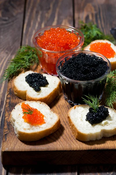 Tradicional caviar vermelho e preto e sanduíches em tábua de madeira — Fotografia de Stock