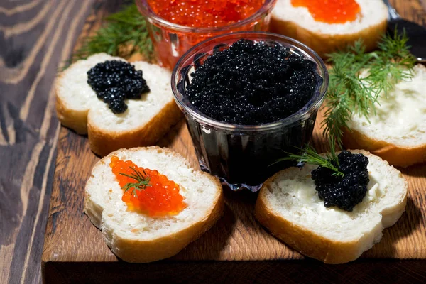 Tradicional caviar vermelho e preto e sanduíches em tábua de madeira — Fotografia de Stock