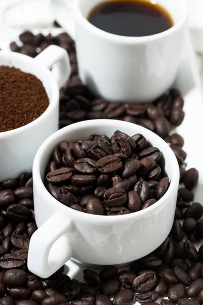 Three types of coffee - ground, grain and beverage in white cups, vertical, closeup