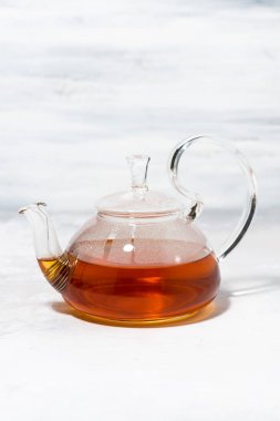 Beyaz zemin üzerinde cam çaydanlıkta çay, dikey