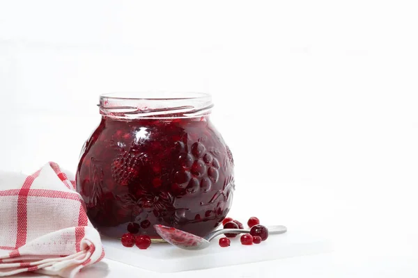 Glass jar of cranberry jam on a white table — Stock Photo, Image