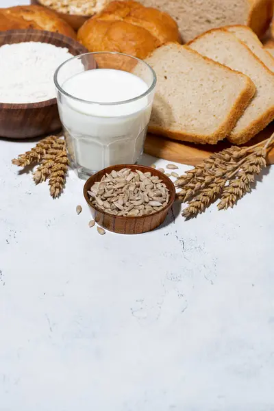Асортимент різноманітного свіжого хліба, склянка молока на білому столі — стокове фото