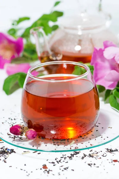 Té fragante con rosa silvestre en una taza de vidrio sobre una mesa blanca — Foto de Stock