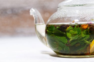 Beyaz zemin üzerinde taze nane ve limon bulunan cam çaydanlık çayı, yatay yakın plan