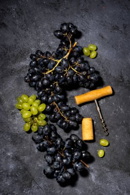 Bir demet taze üzüm ve koyu bir arka planda tirbuşon.
