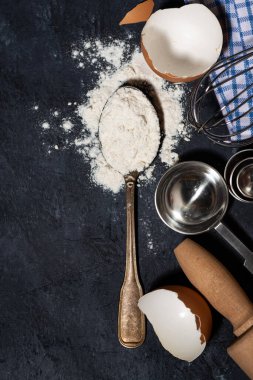 Siyah arka planda buğday unlu kaşık ve pişirme malzemeleri, yakın plan.