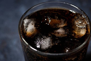 Siyah arka planda buzlu bir bardak Coca Cola, yakın plan.